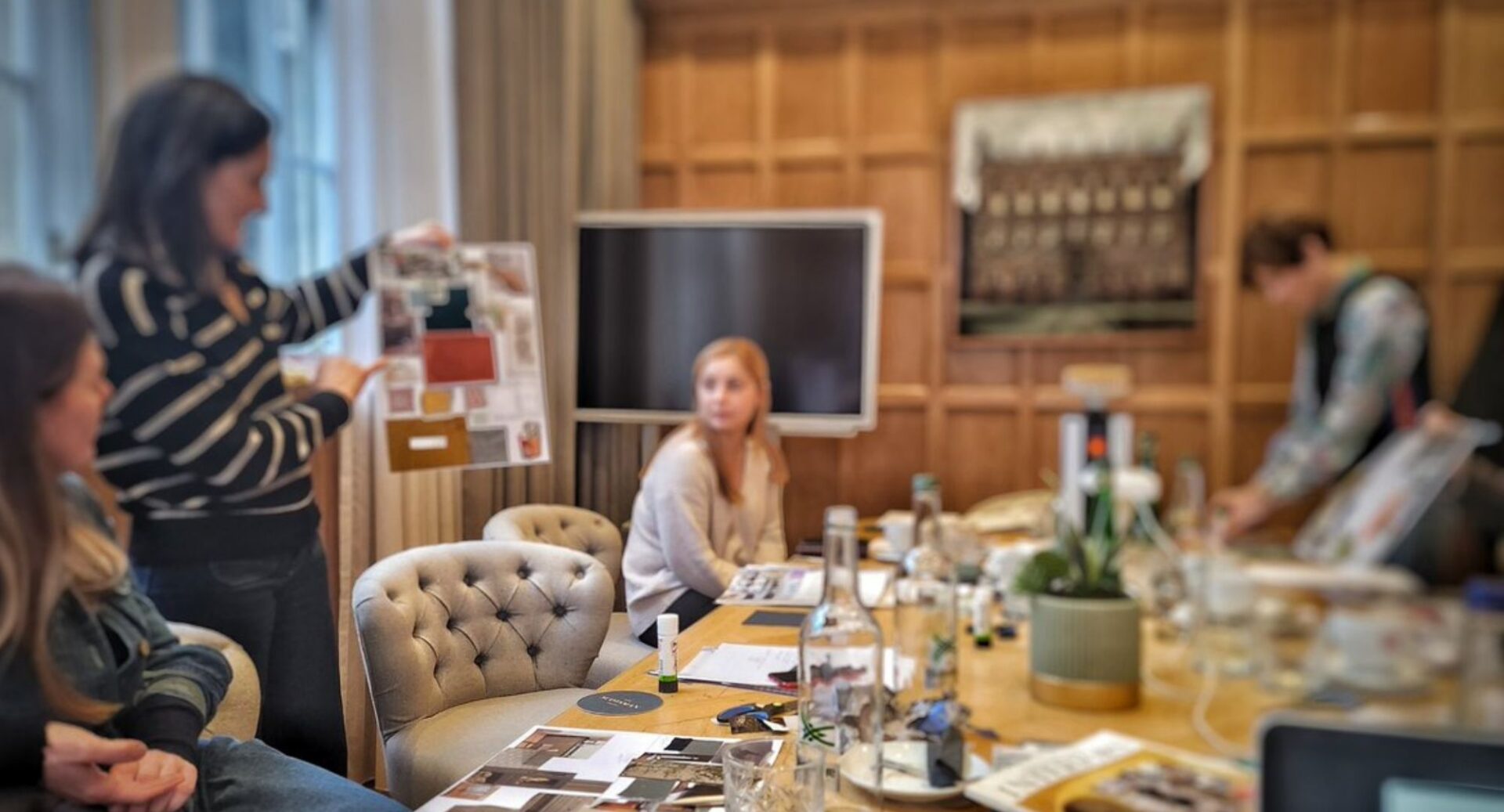 Group of people at a table, which is covered in pictures and photos. A woman at the forefront, holds up poster.