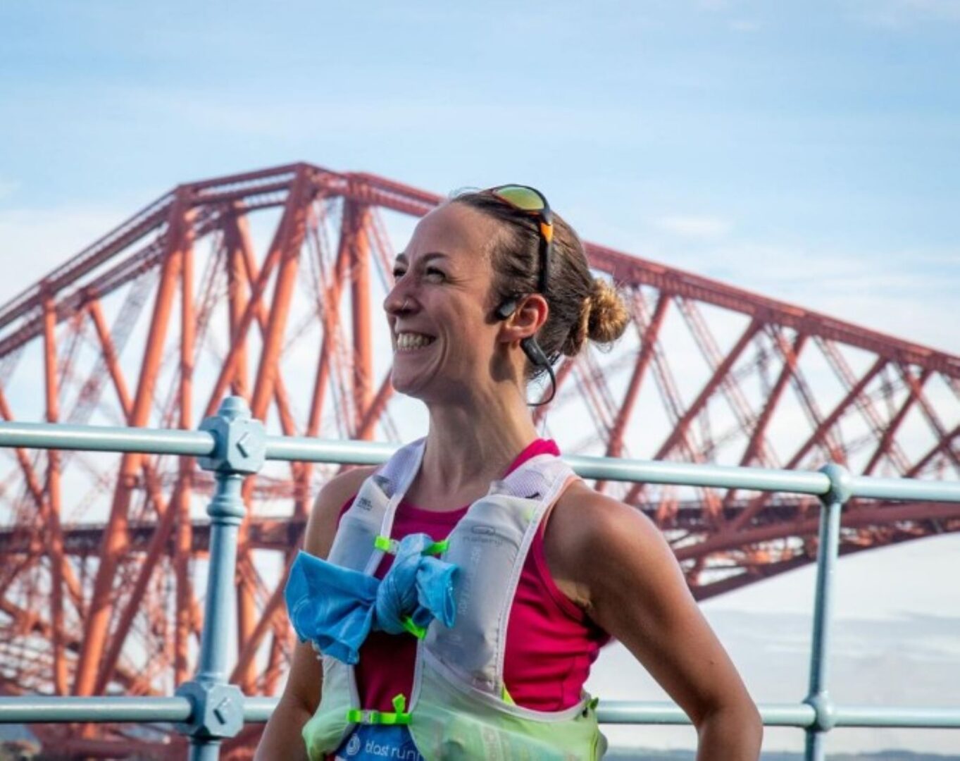 Woman in running gear, standing against a red iron rail bridge.