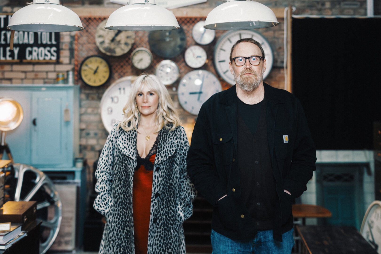 A man and woman stanidng in front of clocks.