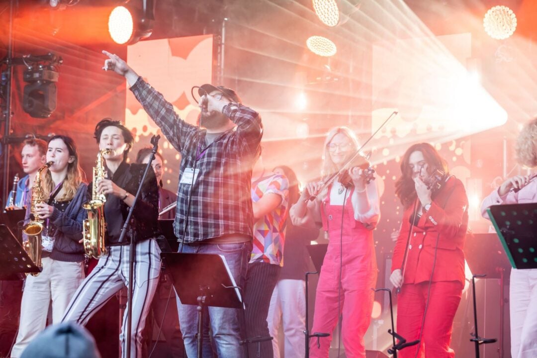 A group of people on a stage, singing and playing a variety of musical instruments.
