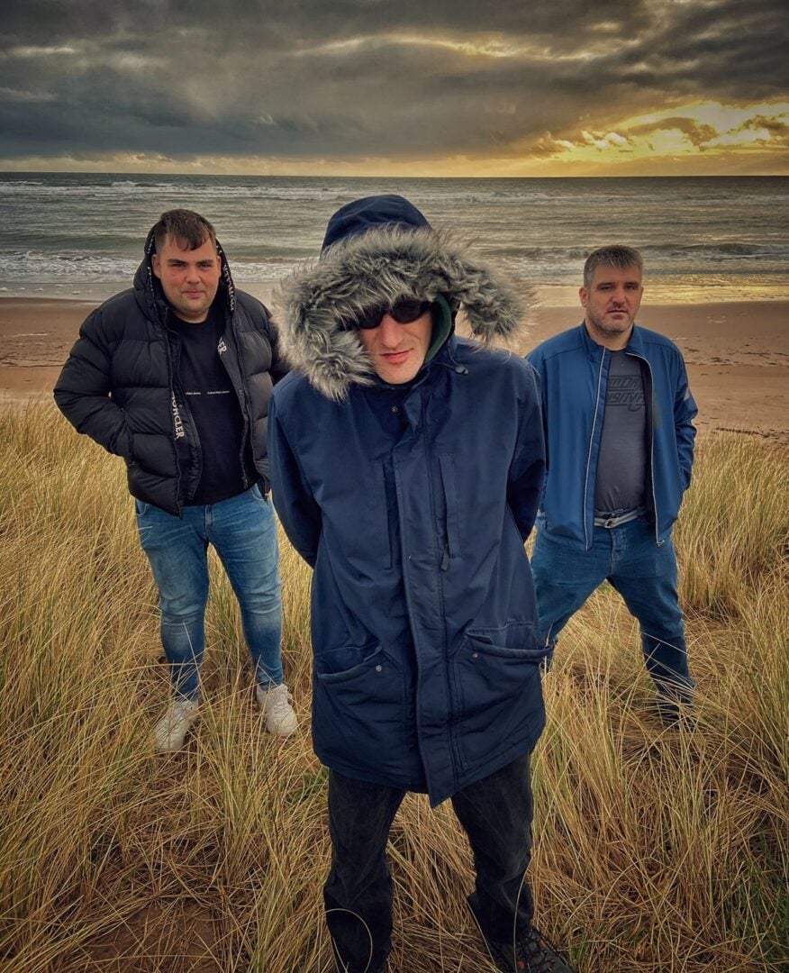 Band Peat & Diesel standing on a sand dune with beach in background and sunset starting.
