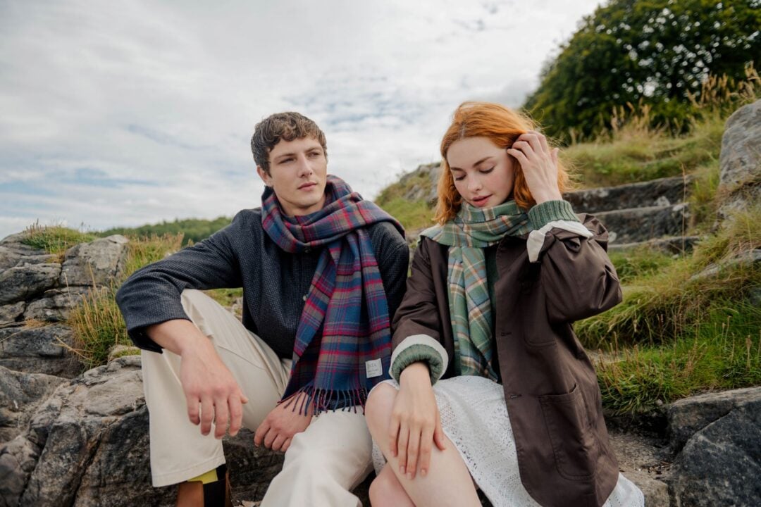 A man and woman wearing tartan scarves, sitting on a rock.