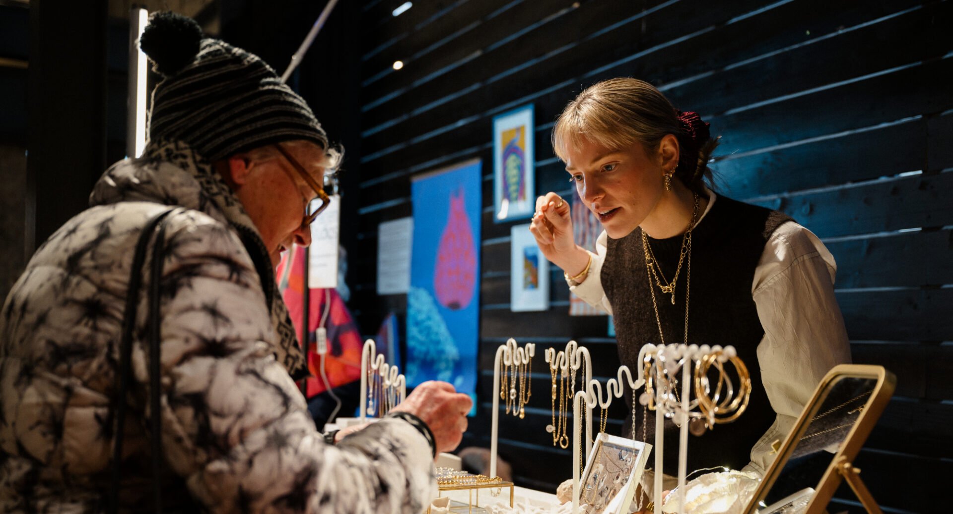 2 woman standing at a stall filled with items of jewellery.