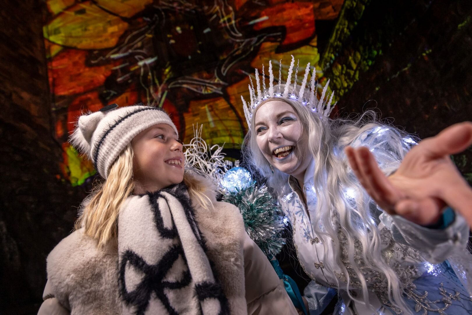 A young girl and a woman dressed as an Ice Queen standing against an illuminated castle wall.
