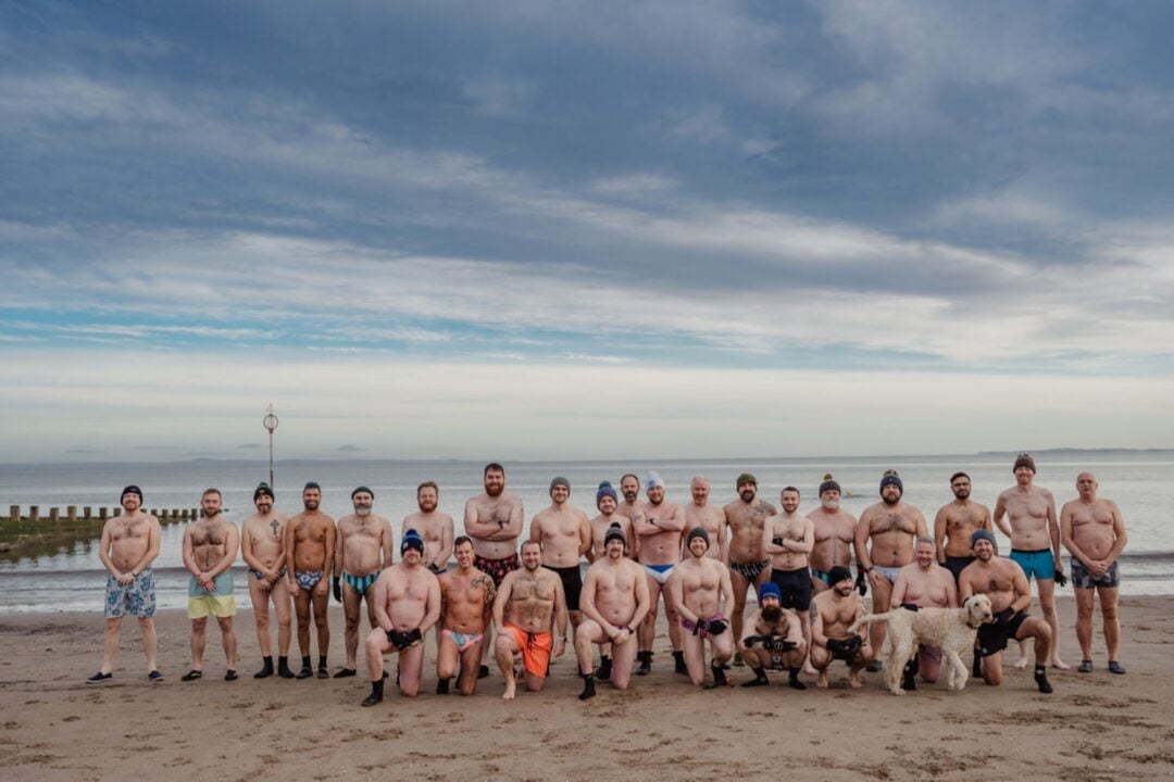 A group of men standing against the shoreline of a beach.