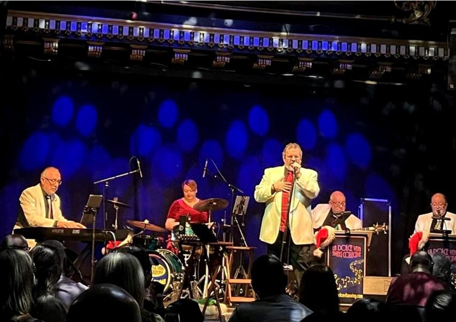 A band of people on a stage, singing and playing a range of musical instruments.