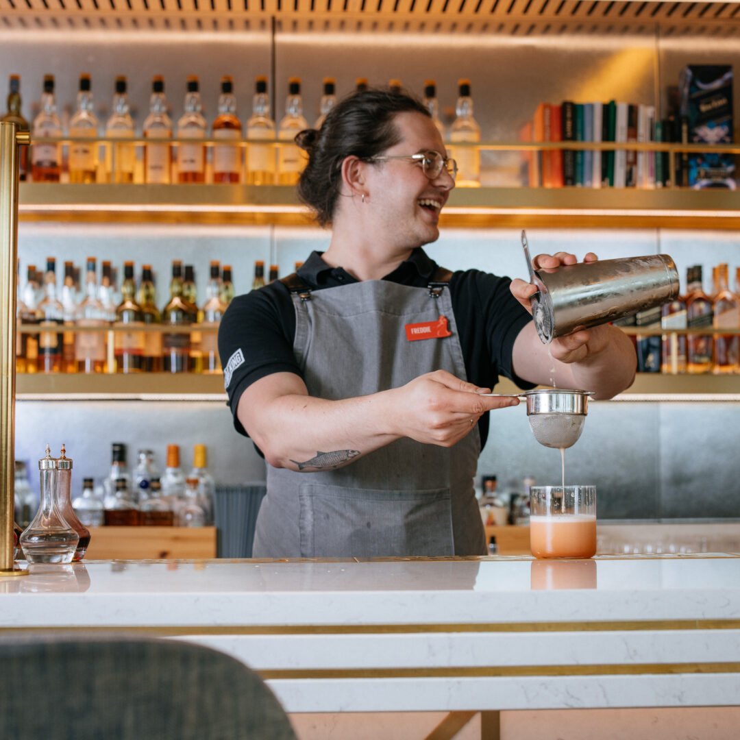 A person standing behind a bar pouring a drink into a glass.
