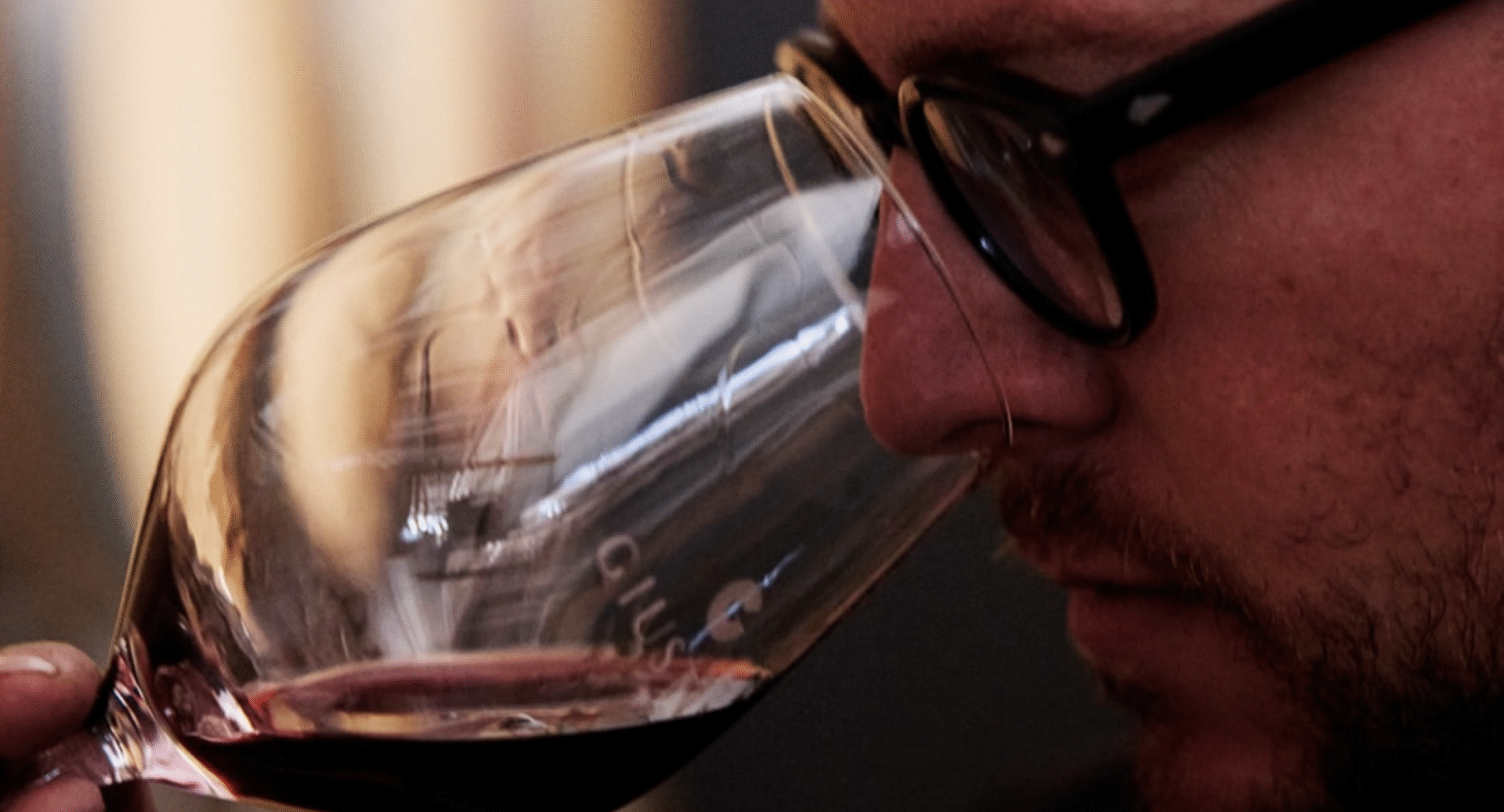 Close-up of a man sniffing red wine from a glass.