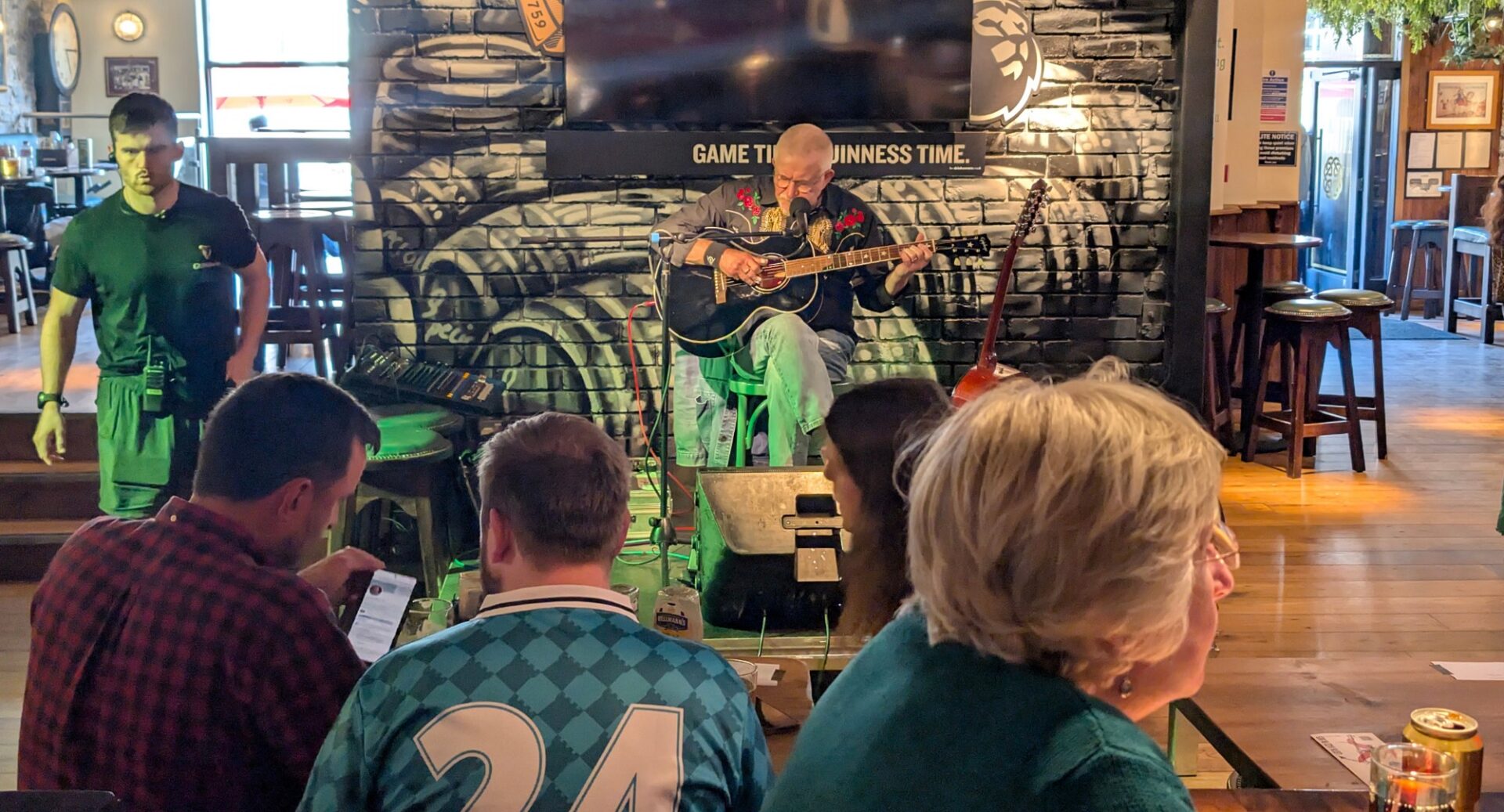 Man sitting down playing a guitar, in front of a group of people.