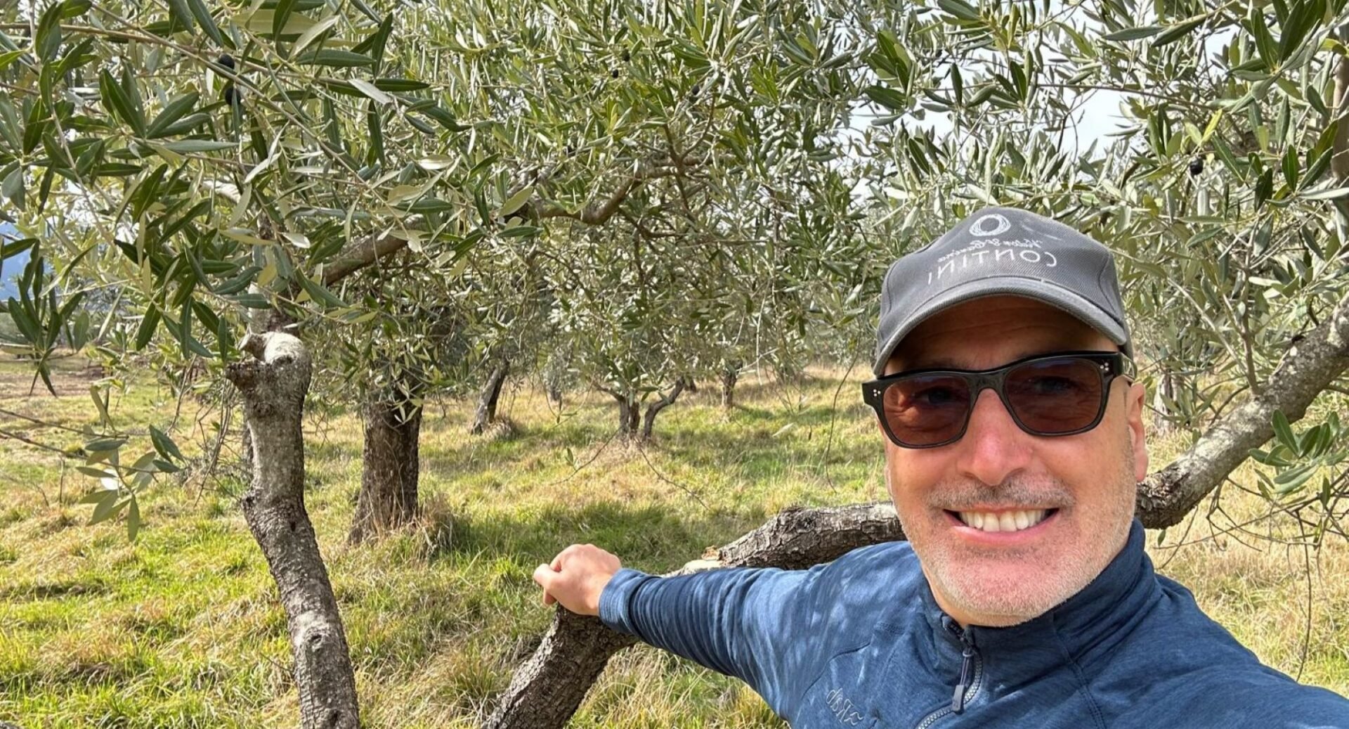 A man standing against a wooded tree area.