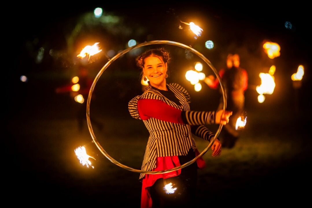 Women standing outside in the dark, swirling a hoop which is lit with fire sparks.