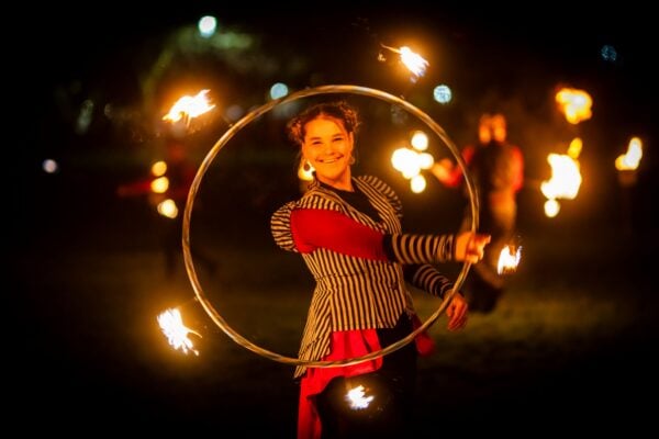 Women standing outside in the dark, swirling a hoop which is lit with fire sparks.