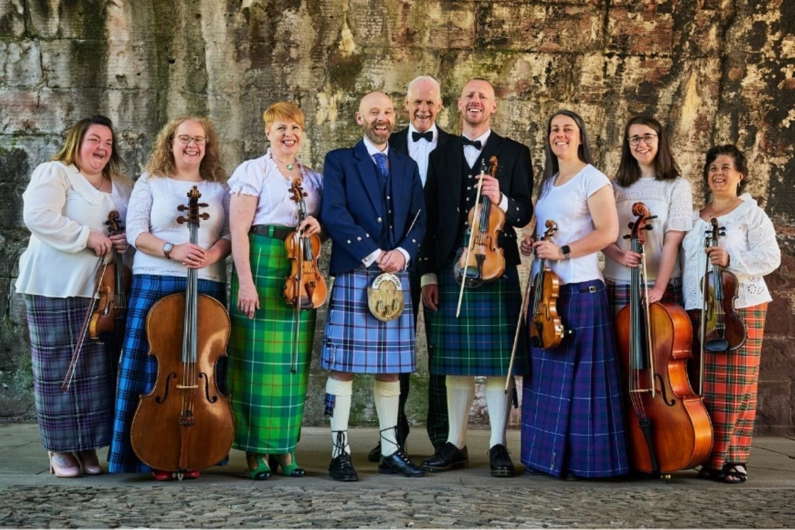 A group of people in traditional Scottish dress, holding fiddles and other stringed instruments.
