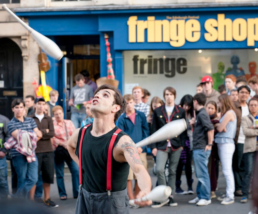 A street performer is surrounded by onlookers as he juggles outside the Edinburgh Festival Fringe Shop.