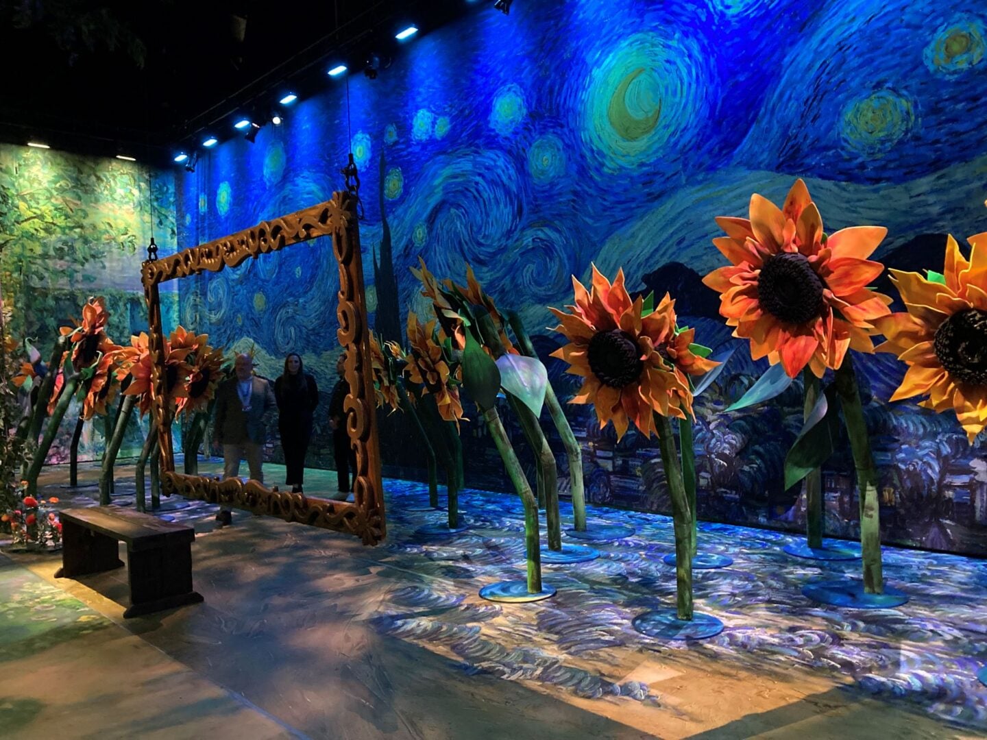 Room filled with over-sixed sunflowers, and a wall painted in shades of dark blue with swirling movements.