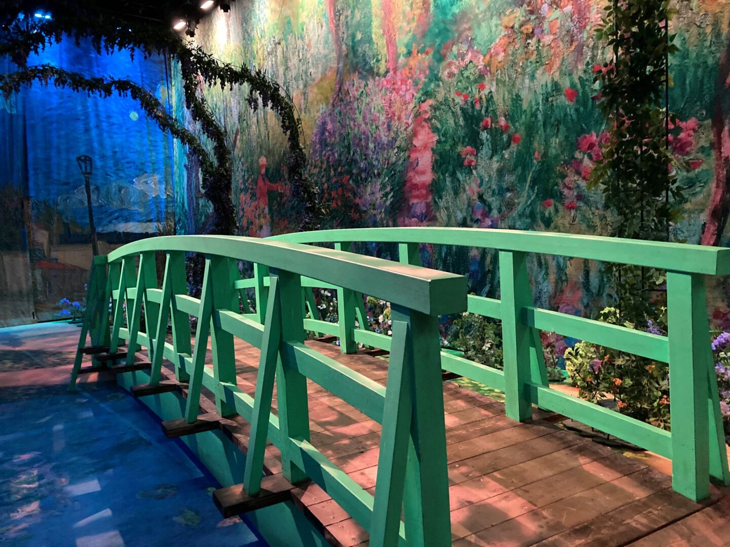 A green bridge, overlooking a river and wall painted with colourful flowers.