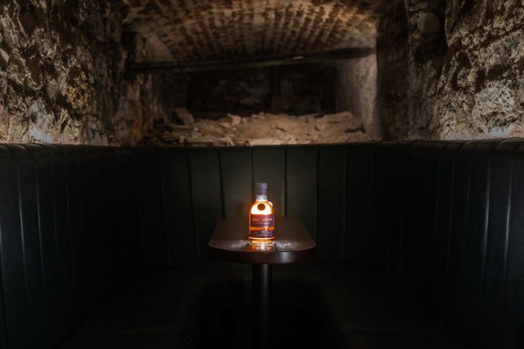 An underground space, with a table and bottle of whisky.