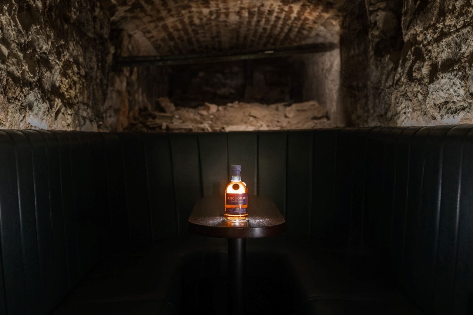 An underground space, with a table and bottle of whisky.
