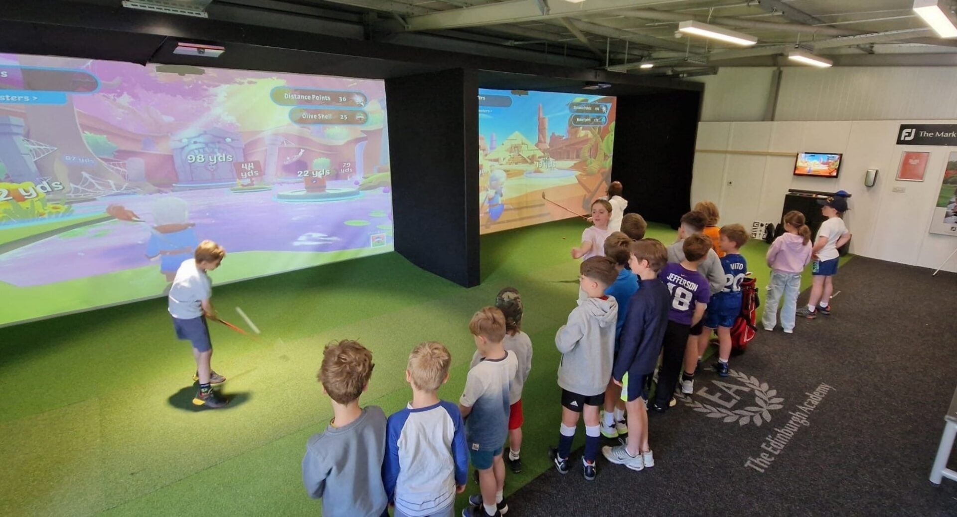 A group of young children playing a on a golf simulator.