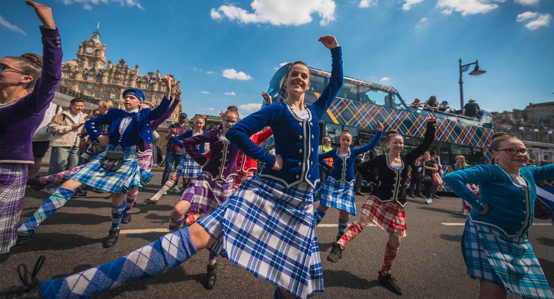 A group of people wearing traditional Scottish dress, and dancing a Highland jog.