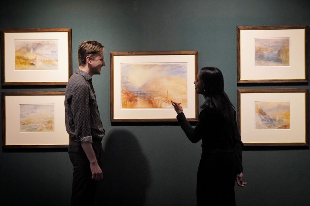 A man and woman looking at a display of paintings on a wall.
