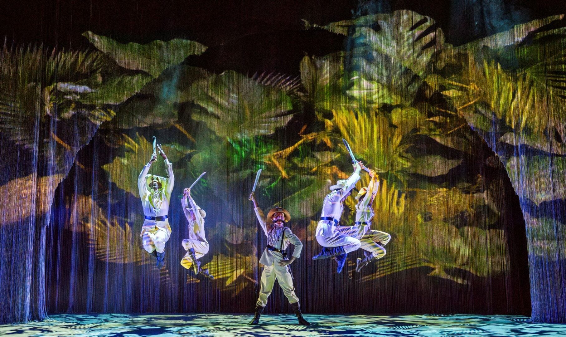5 people dancing on stage, against a jungle-like background.