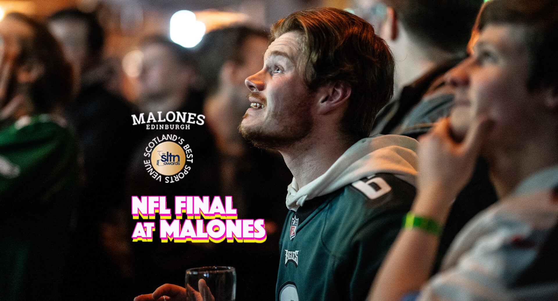 2 men wearing NFL shirts looking up at a screen.