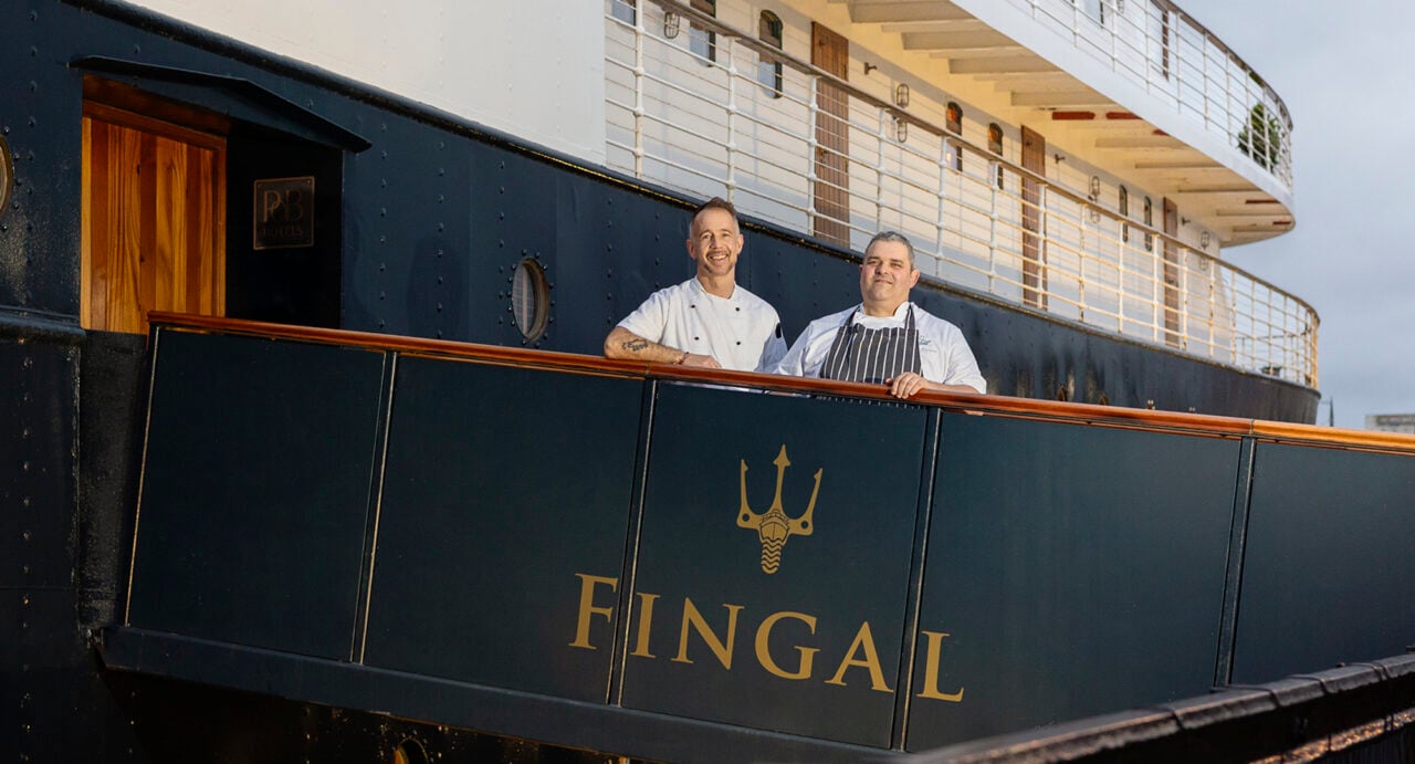 2 men in chefs uniforms standing onboard a ship.