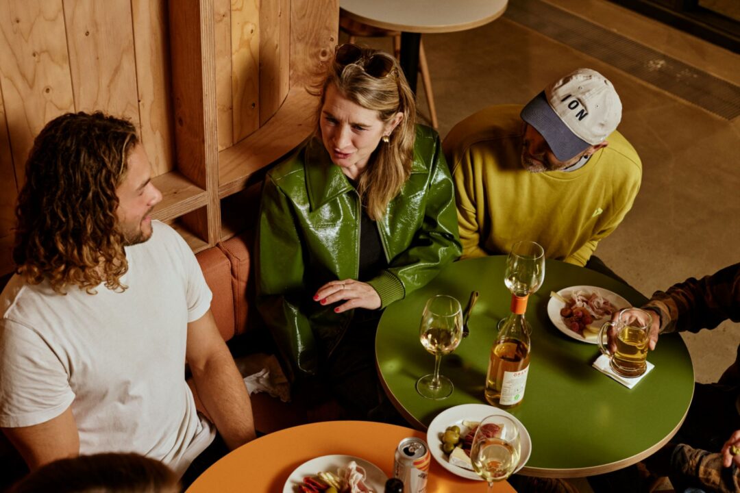 A group of people seated around a table. On the table are a bottle of wine, glasses and plates of food.