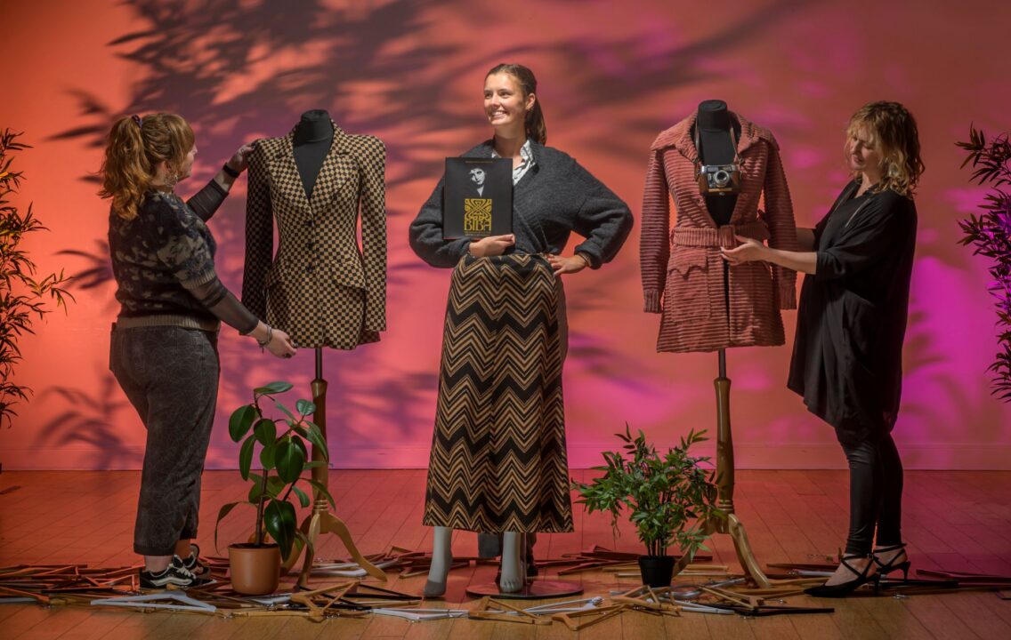 3 woman setting up displays of clothing on mannequins.
