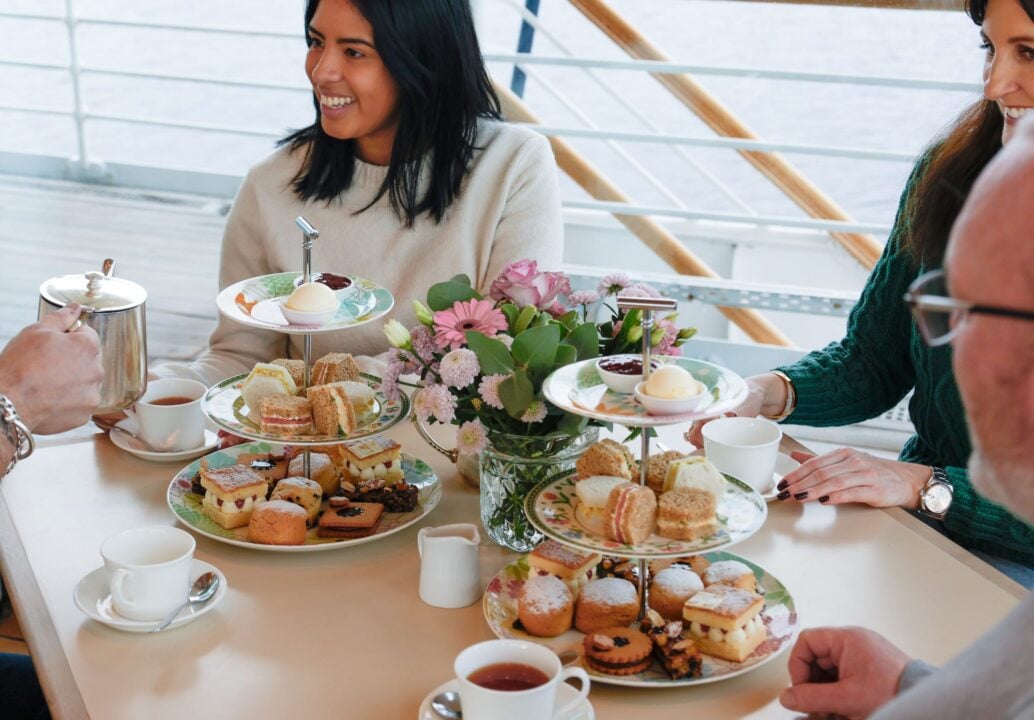 Group of people seated at a table, set with tiers of afternoon tea.