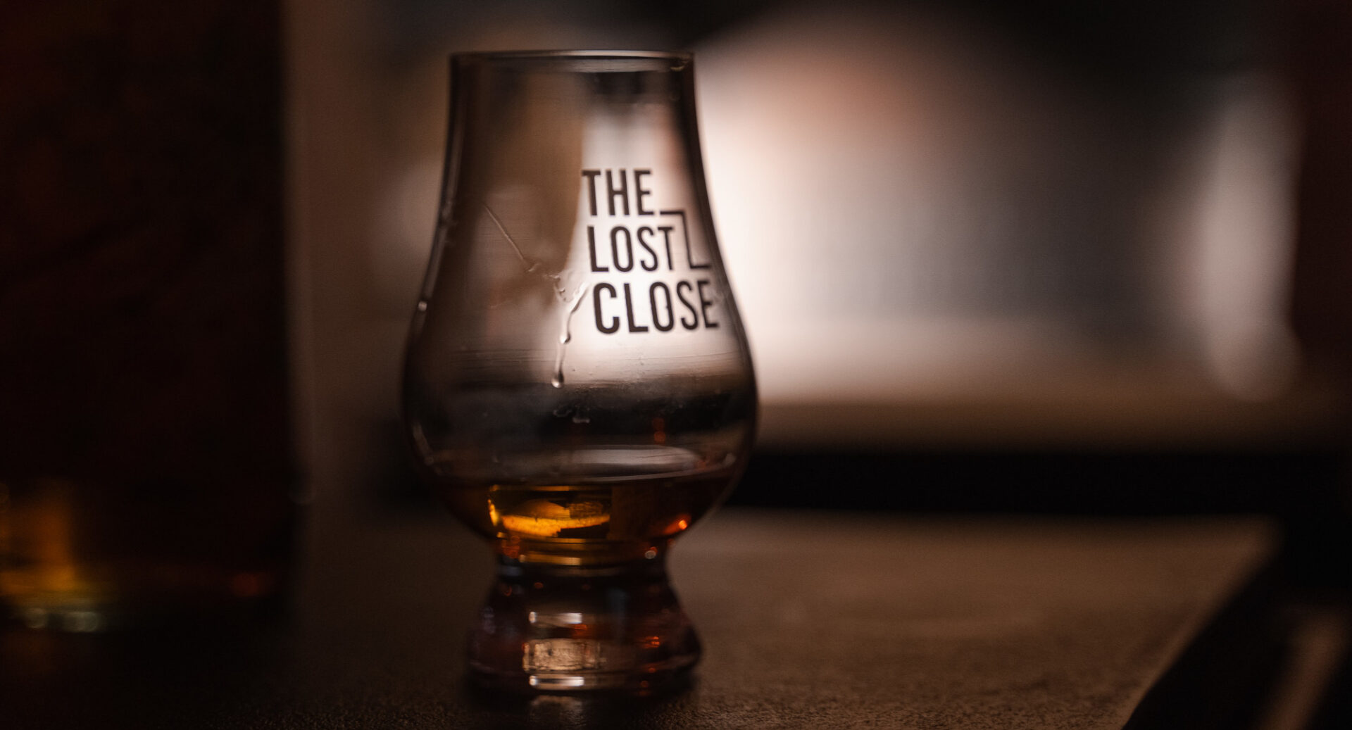 Close-up of a filled whisky glass, with the words, The Lost Close, on the side.