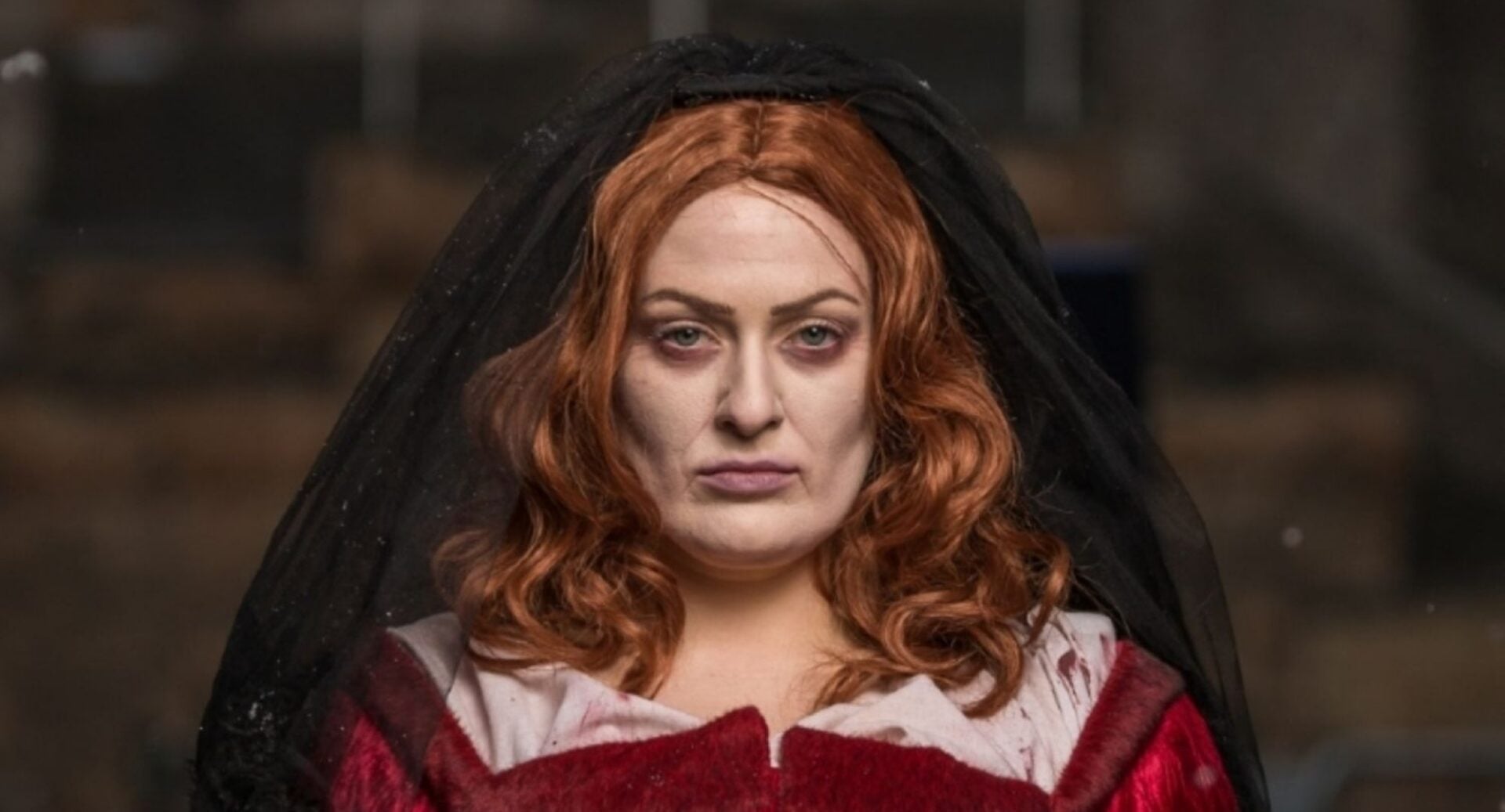 Portrait image of a woman in a red and white dress and a black headscarf.