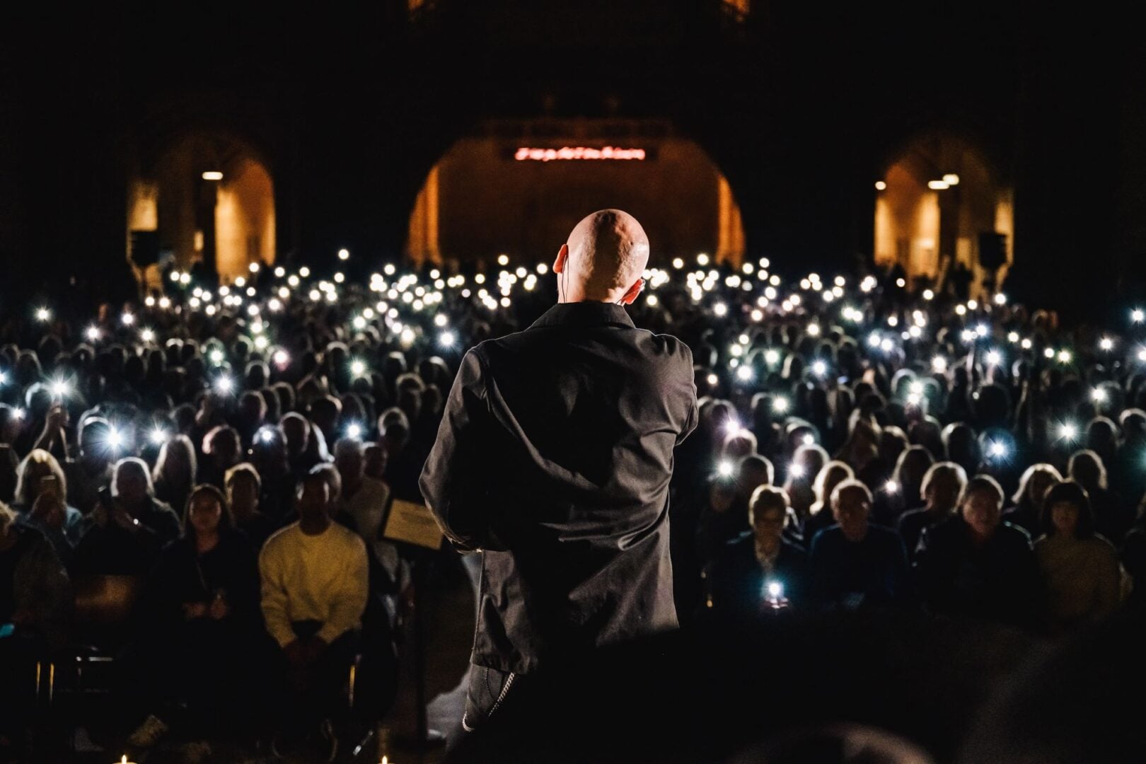 A person, with their back to the camera, performing on stage on front of an audience.