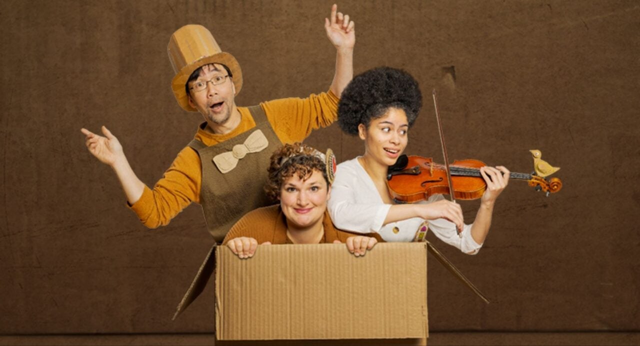 3 people, one holding a violin, coming out of a cardboard box.