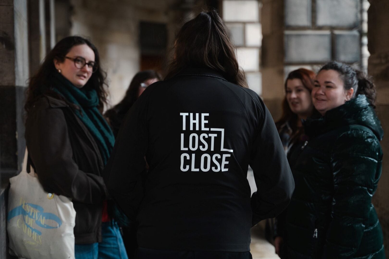 Person with their back to the camera (and wearing a jacket with The Lost Close on the back) taking to a group of people.