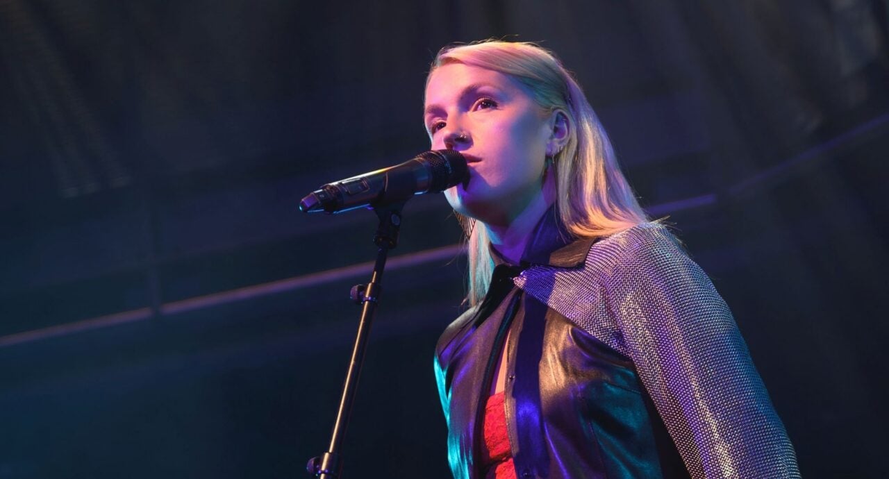 A woman with shoulder-length blonde hair singing into a microphone.