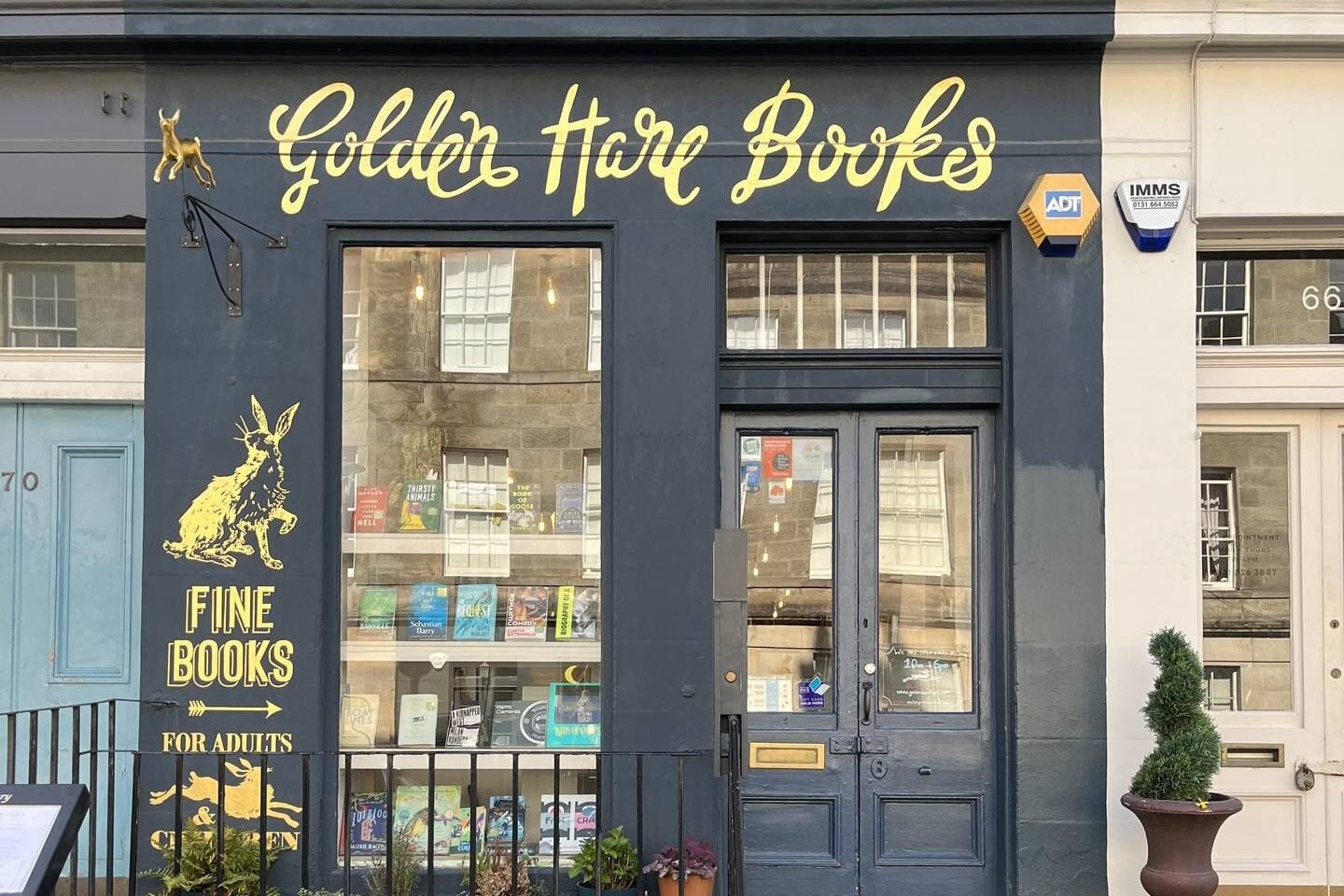 Dark blue shop front with beautiful golden lettering that spells Golden Hare Books. Large window with four rows of books displayed.,© Golden Hare Books 2023