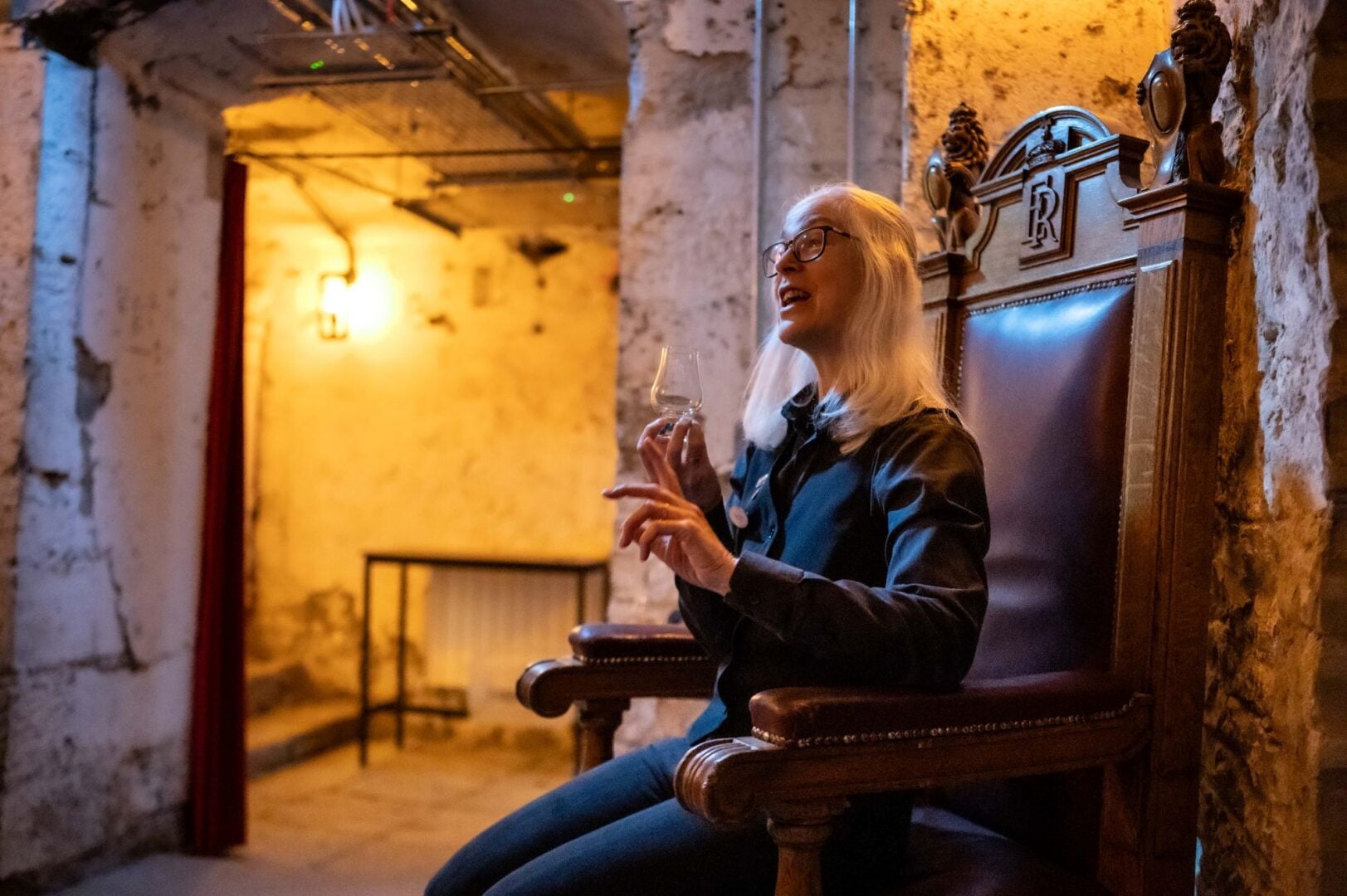 Woman sitting on a throne-type wooden chair, talking.