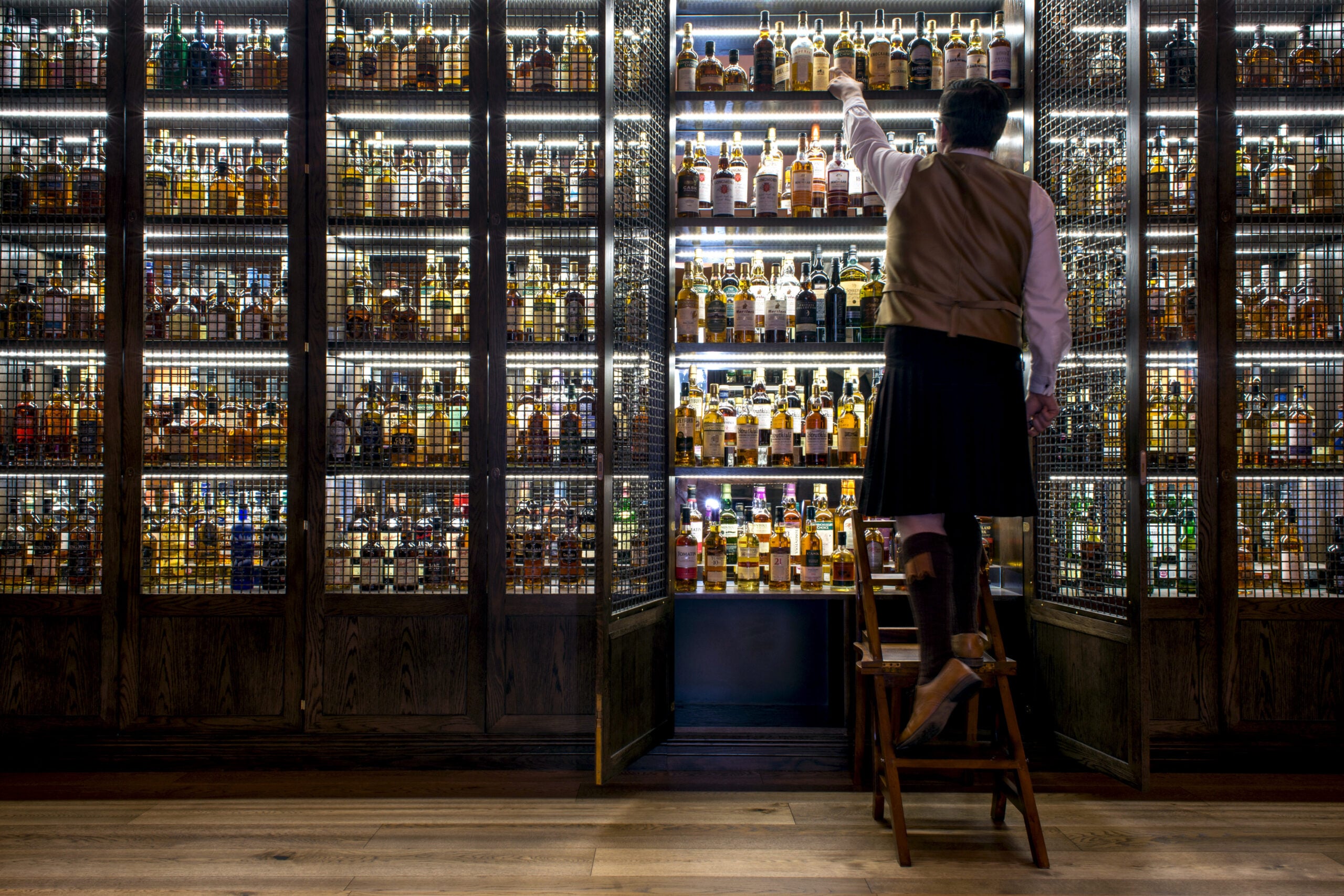 Staff member in kilt reaches into whisky cabinet at SCOTCH bar located in The Balmoral