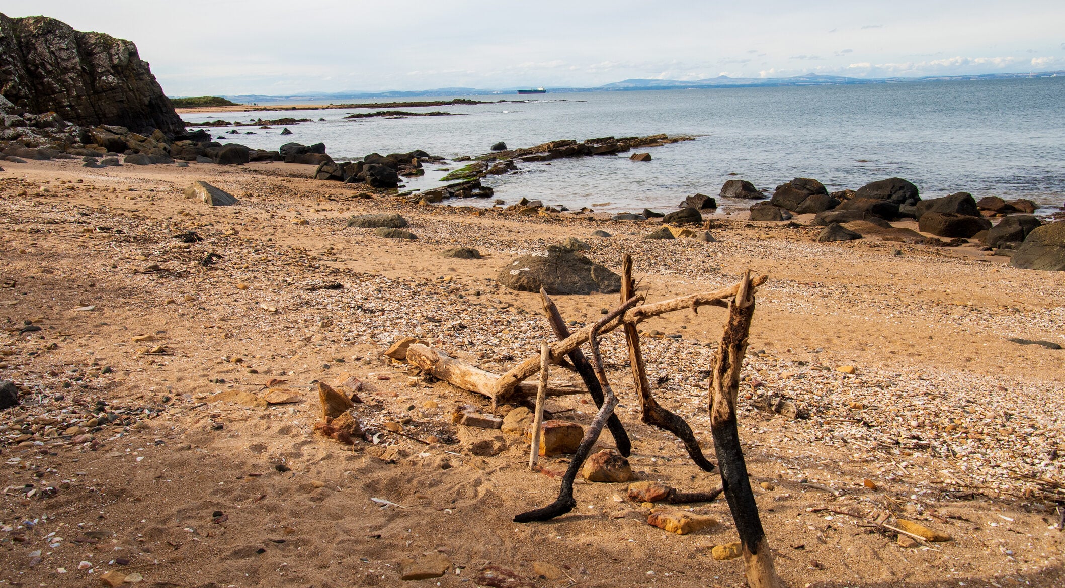 Sandy beach on the east coast of Scotland, rocks and cliffs, sticks sculpture, water of the Firth of Forth