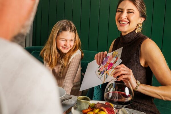 A woman and young girl sitting at a dining table. The woman is opening a gift card.