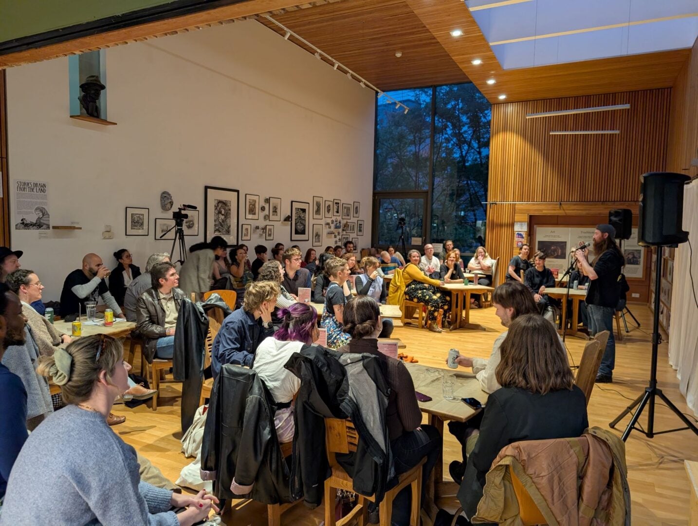 Group of people in an indoor hall, watching a person perform on stage.