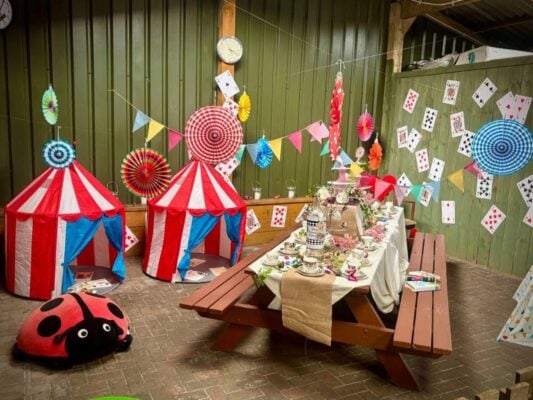 A room set up for tea party, with a bench table set with food and cups and saucers.