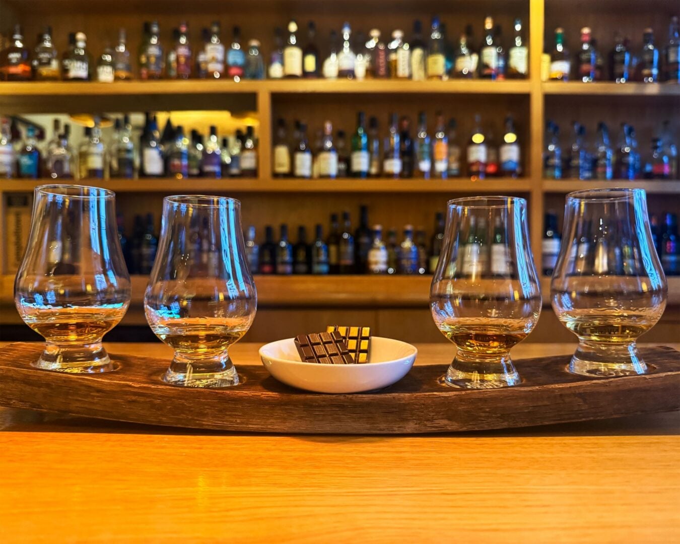 Close-up of 4 filled whisky glasses, and 2 bars of chocolate.