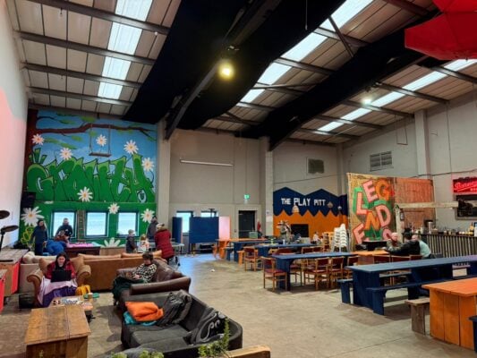People sat around soft seats and bench tables in a warehouse-style building.