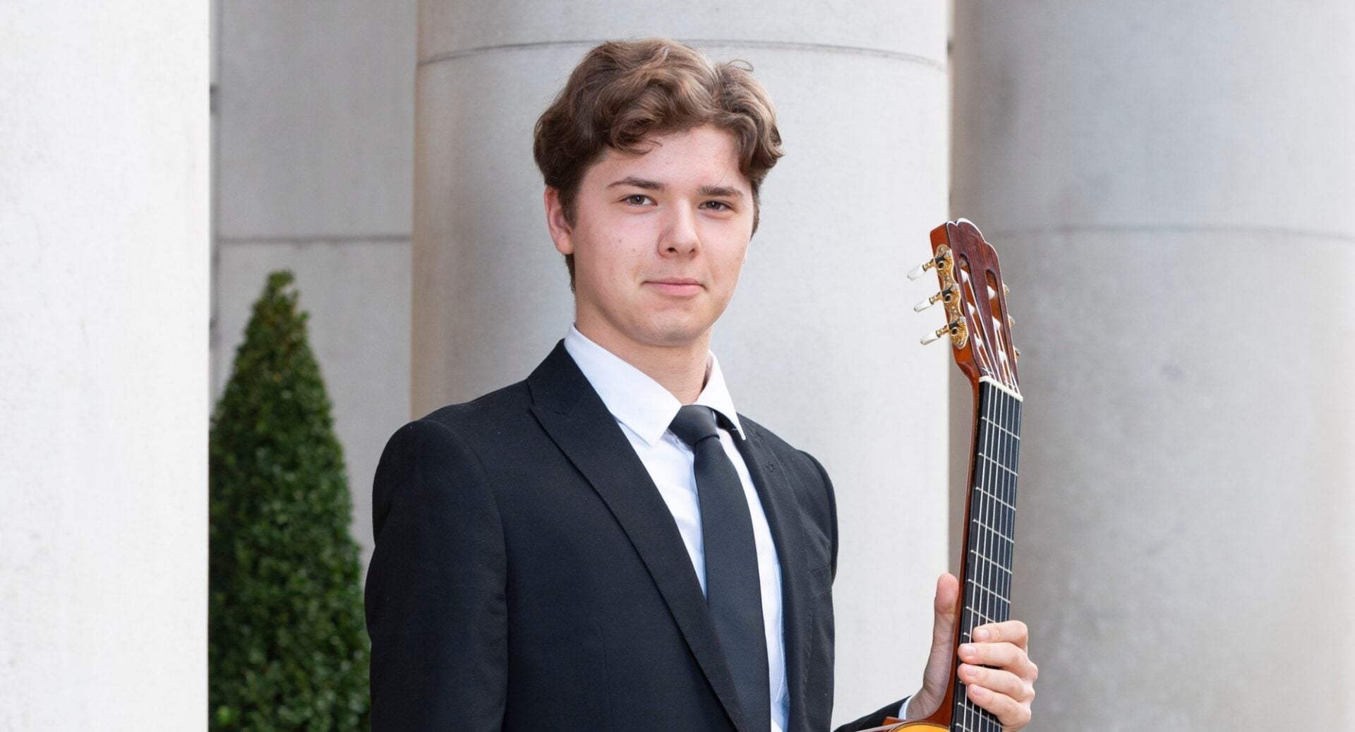 Man in dark suit holding a musical instrument.
