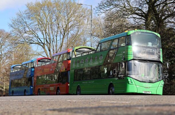 Three of Edinburgh Bus Tour buses waiting at stop under trees.