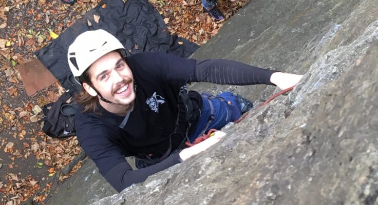 Climber looking up at camera while climbing cliff wall