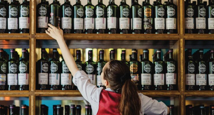 Bar lady reaching a whisky bottle of a packed shelf of whiskys.
